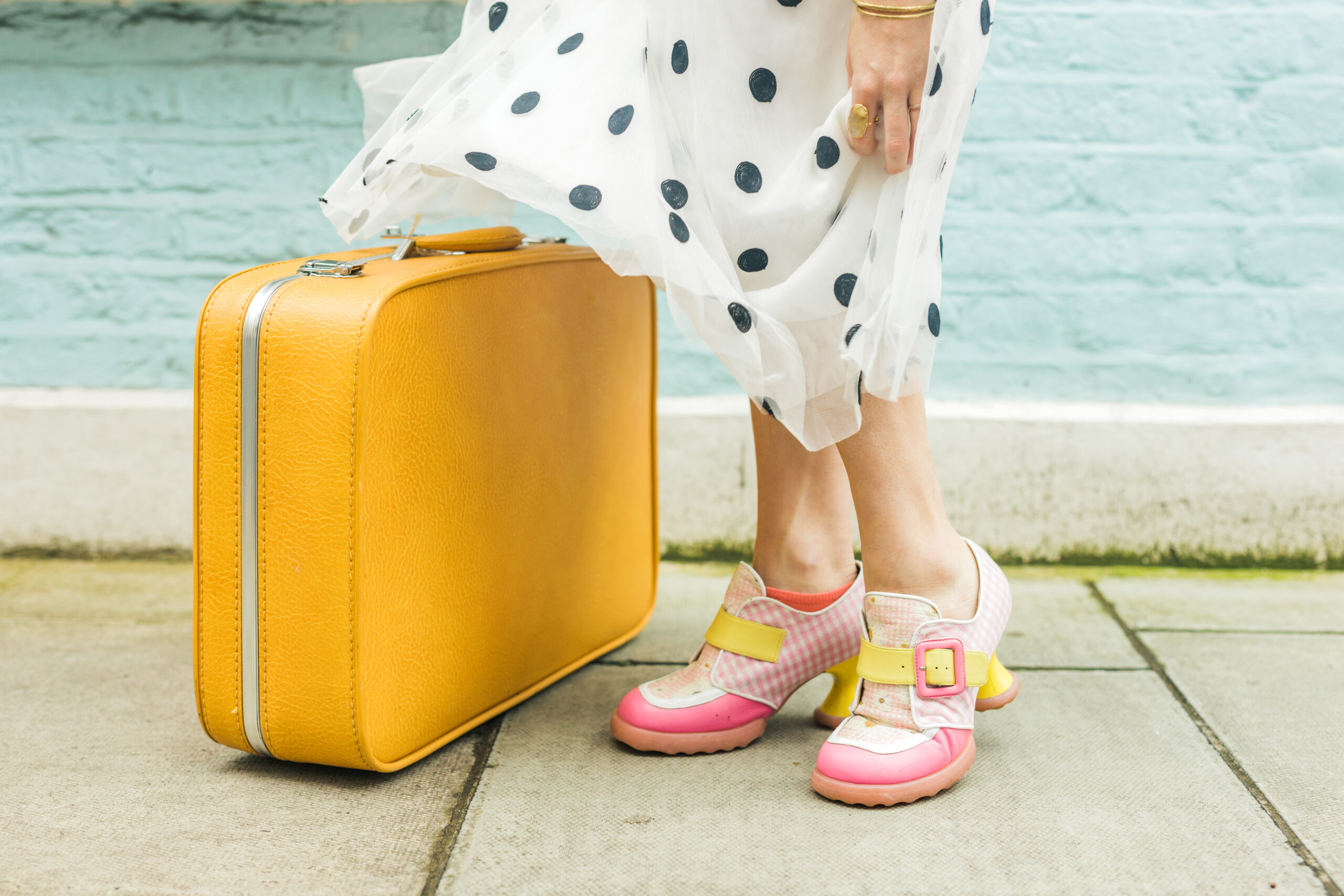 Helena Woods locational astrologer and astrocartographer planning travels with yellow suitcase and polkadot dress